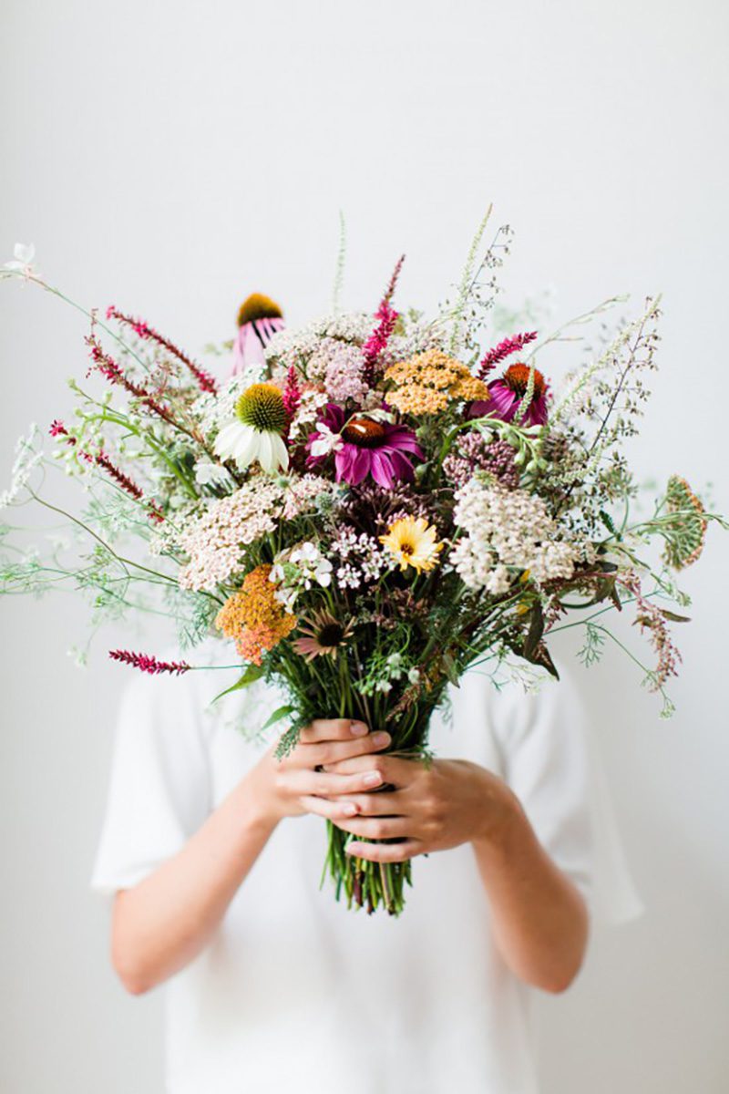 person in a white t-shirt holding a bouquet of wildflowers