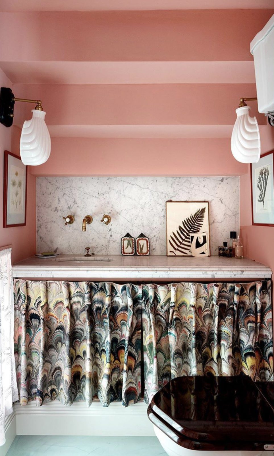 Pink bathroom with marble countertop and backsplash, artwork, and curtain underneath the sink