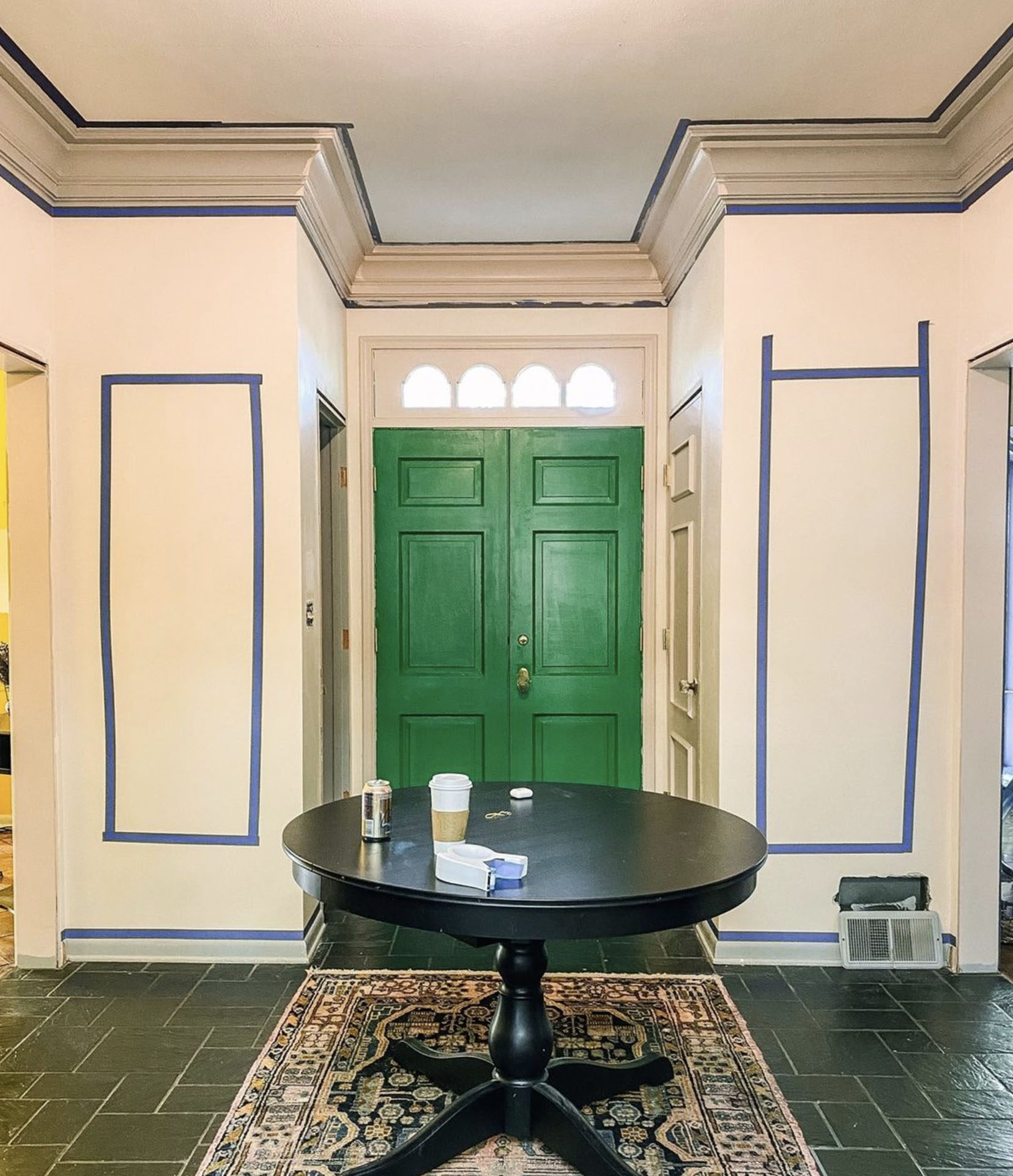 The entryway of a home has a kelly green front door and painter's tape on the walls where picture molding will be hung
