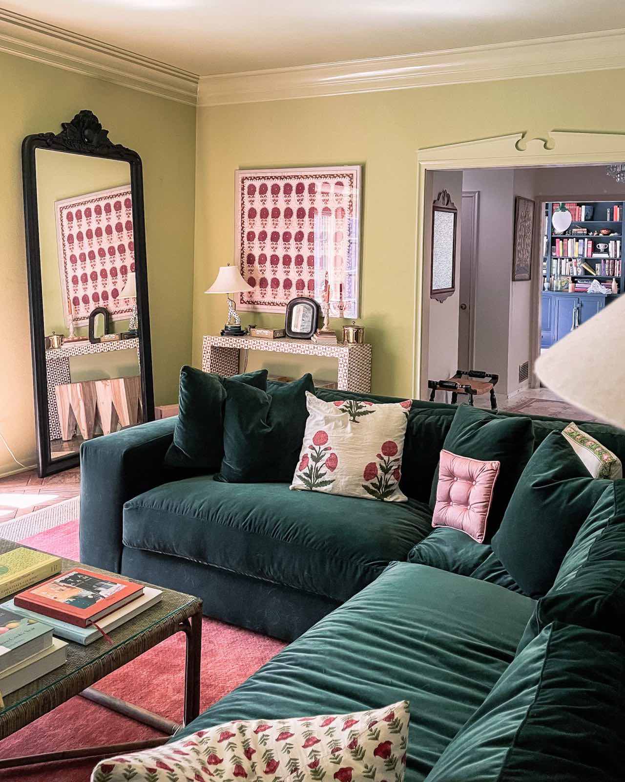 A green family room with a red rug and green velvet corner sectional
