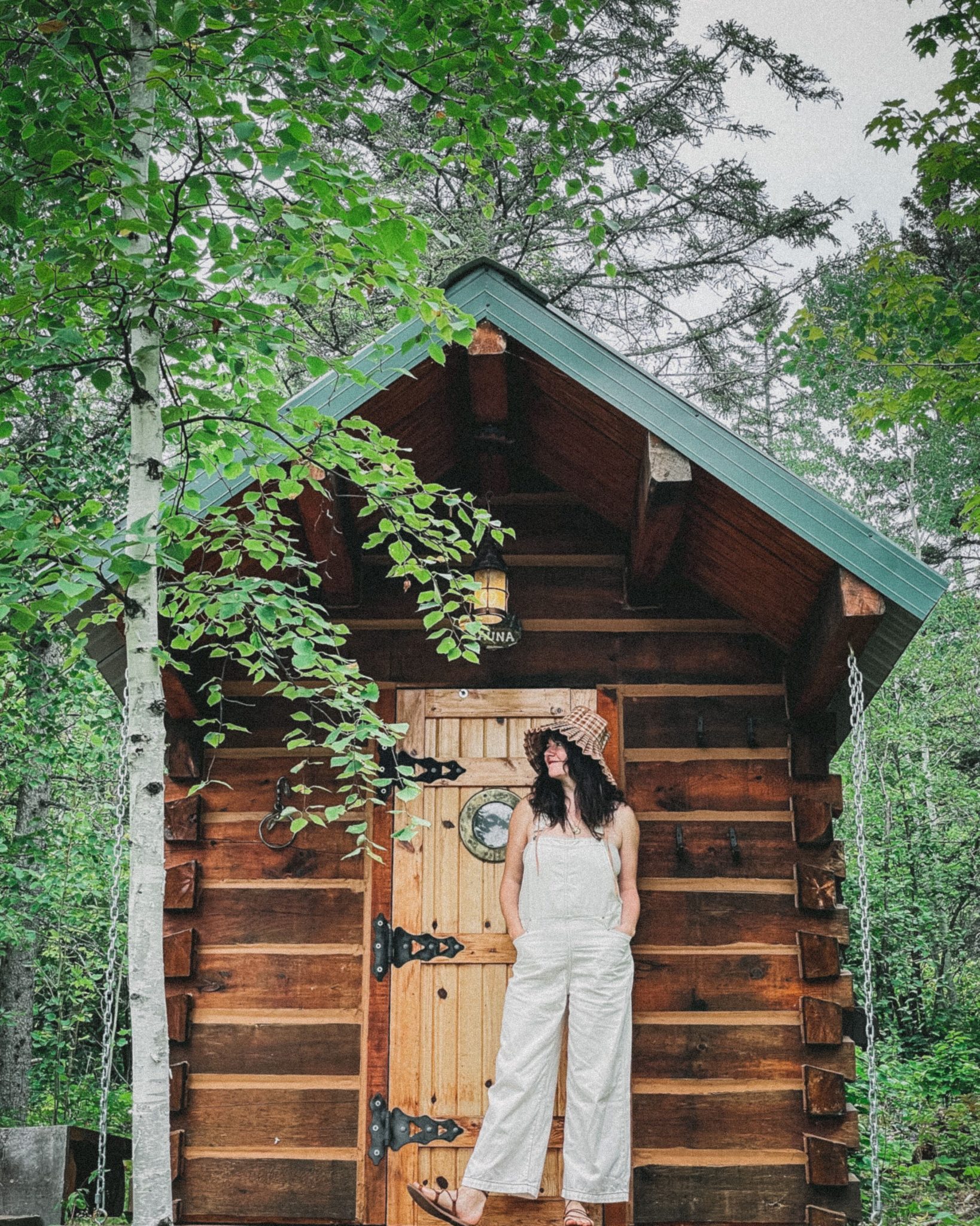 Woman wearing white overall, hat, and sunglasses standing in front of a cabin