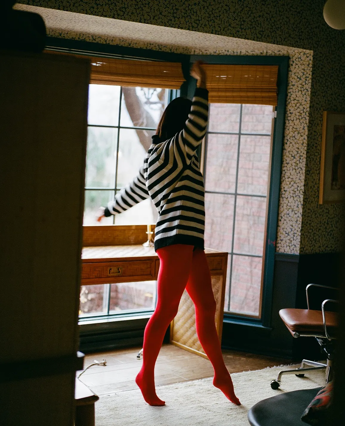 A woman wearing red tights and a striped top dances in her home office