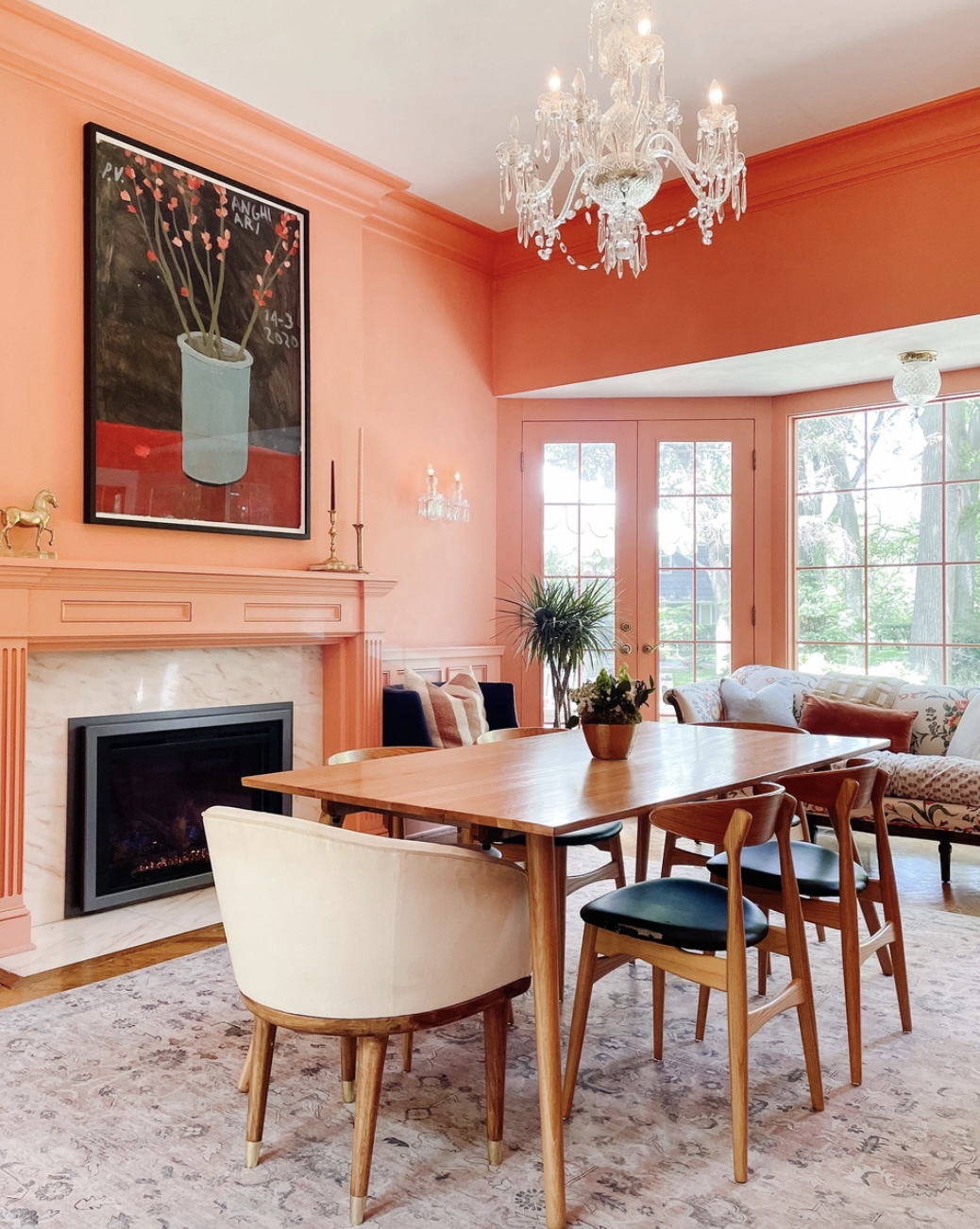 A peach dining room is grounded by a blush-colored Loloi rug, which is topped with a midcentury modern wood dining table and six dining chairs.