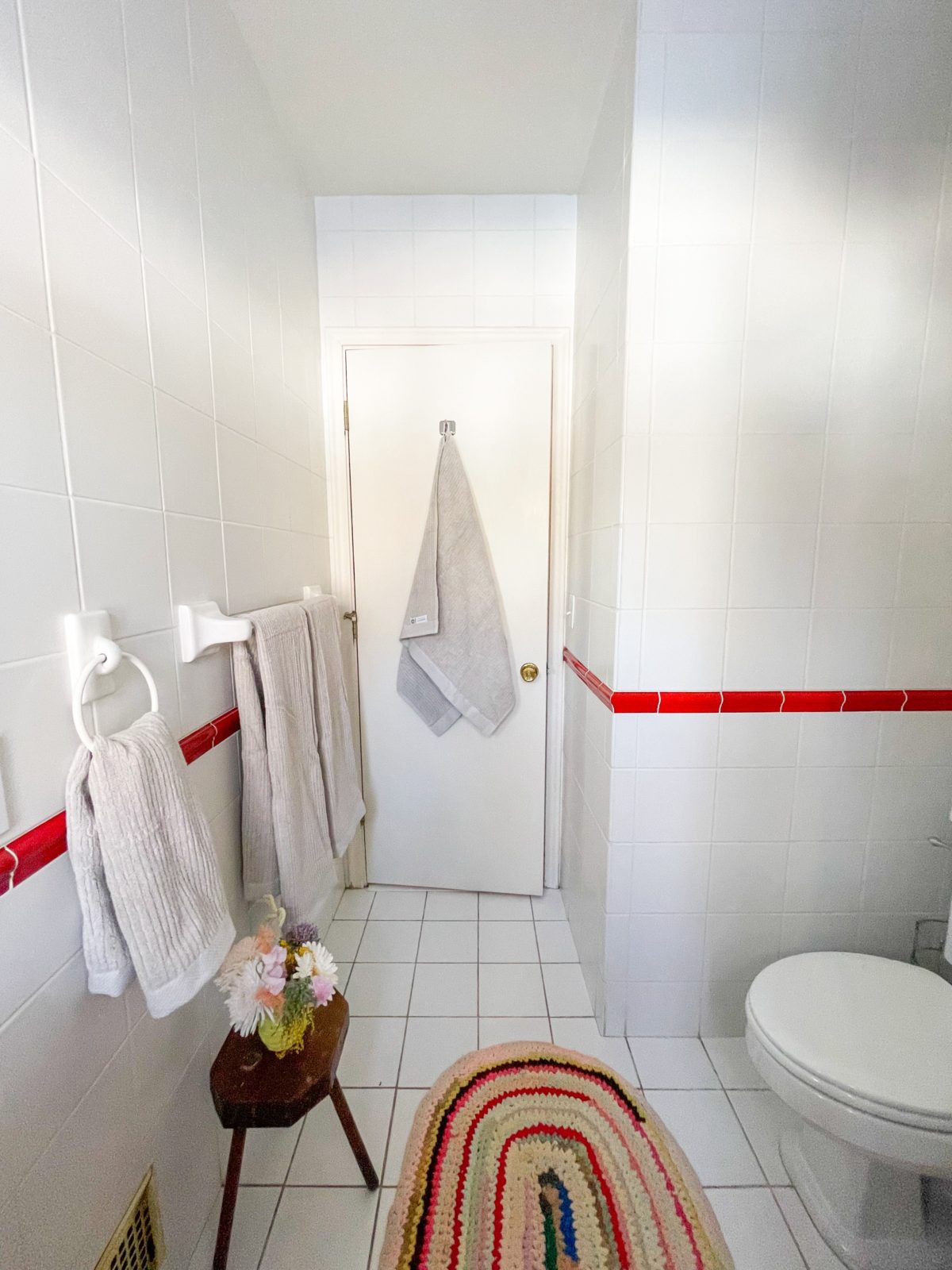 White tiled bathroom with Organic cotton bath towels from Avocado  hanging on bars and on a hook on the back of the door. 