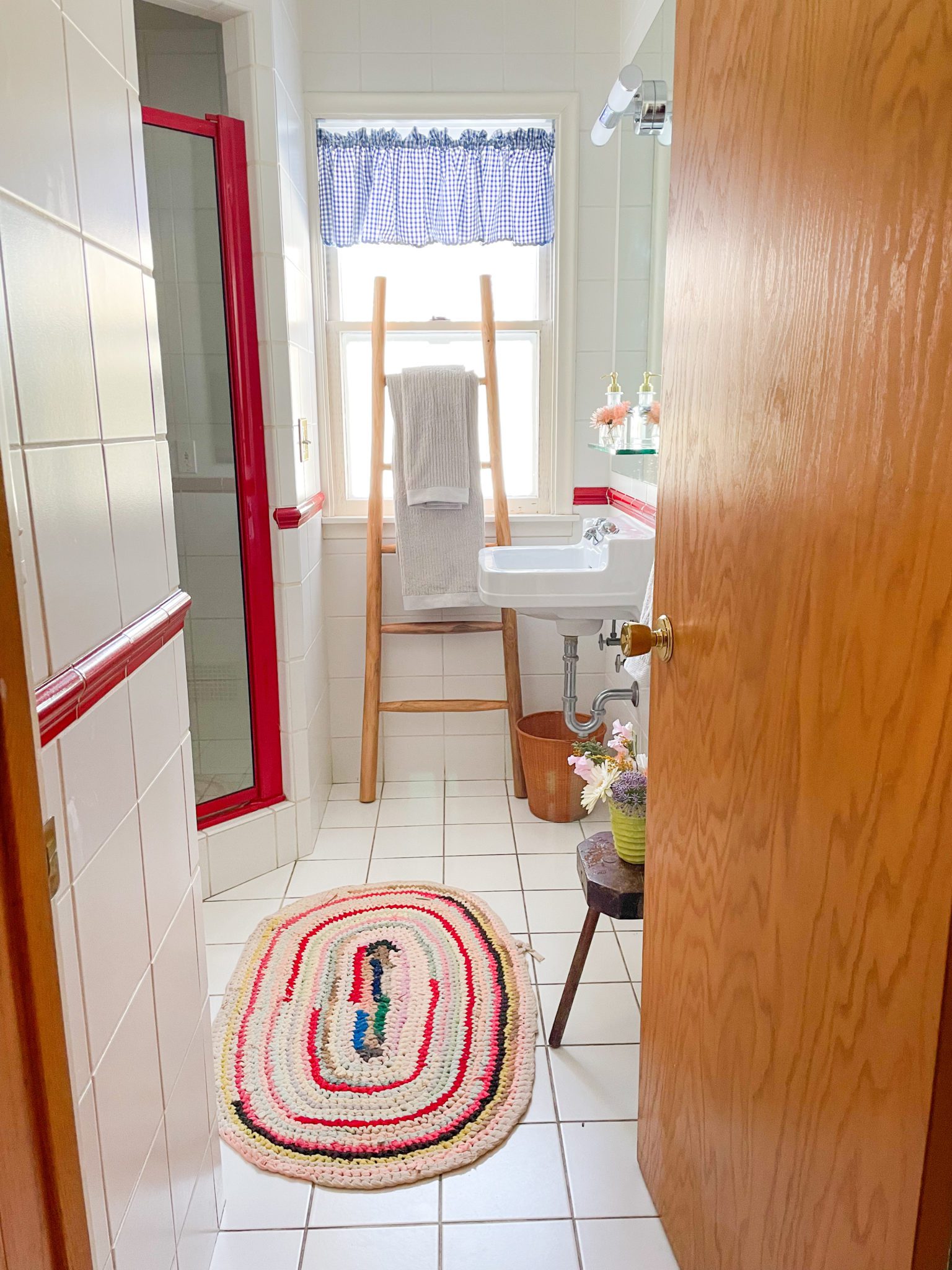 White and red bathroom, with a colorful rug and curtains. Organic cotton bath towels from Avocado hang on a rack.