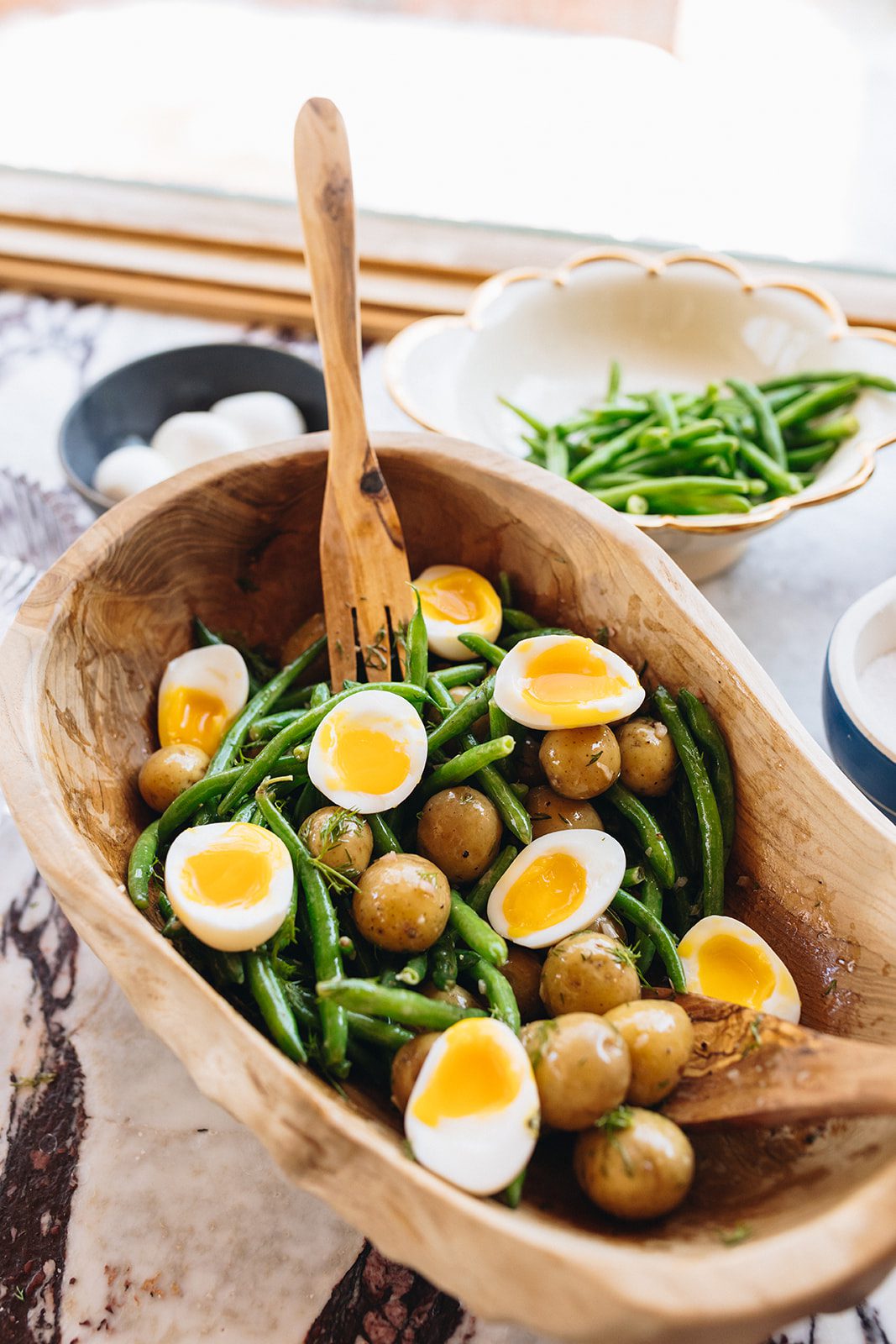 French green bean potato salad with medium-boiled eggs in a wood serving bowl on a marble countertop.