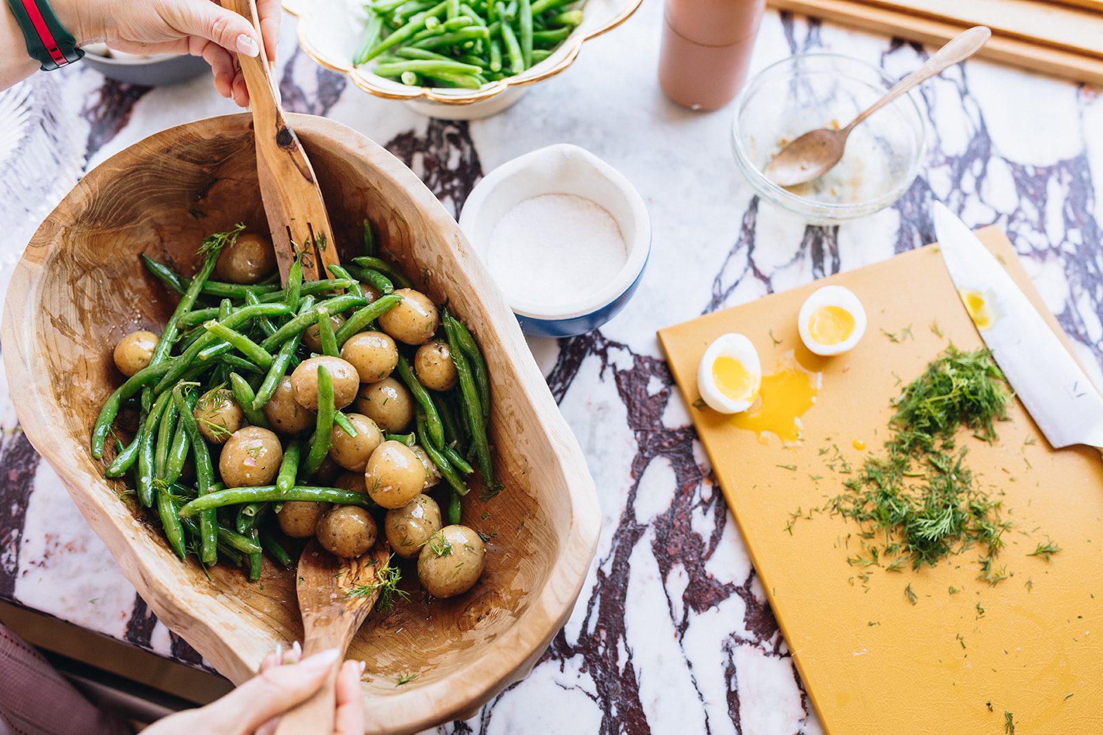 French green bean potato salad in a wood serving bowl on a marble countertop.