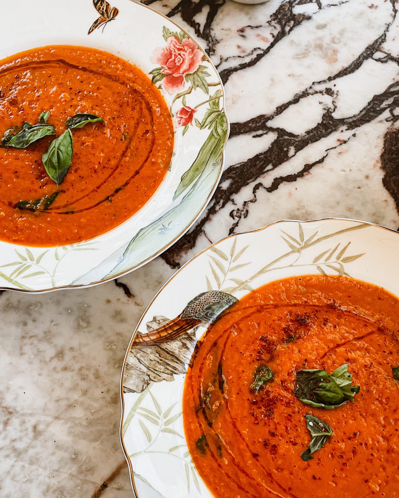 Two bowls of bright red, tomato soup on a marble countertop. 