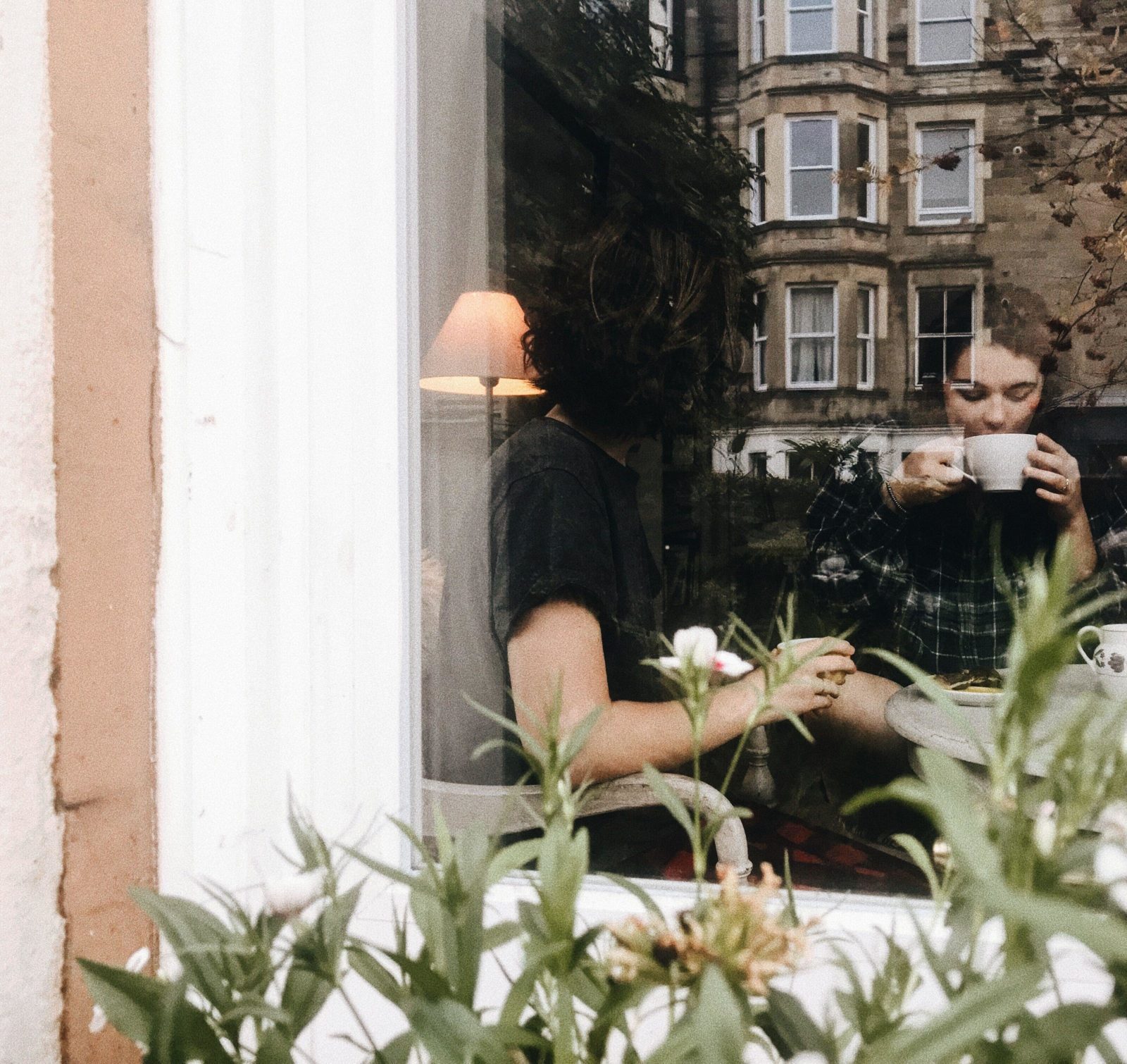 Two people sitting at a table in a coffee shop with flowers outside the window