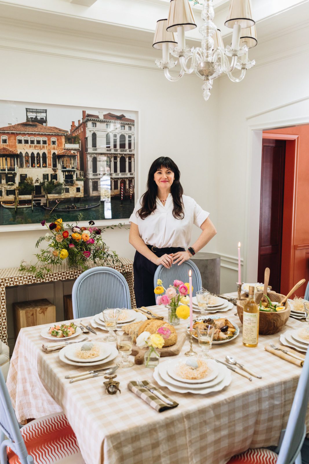 Woman standing behind a fully set and decorated spring luncheon tabletop, smiling at the camera. 