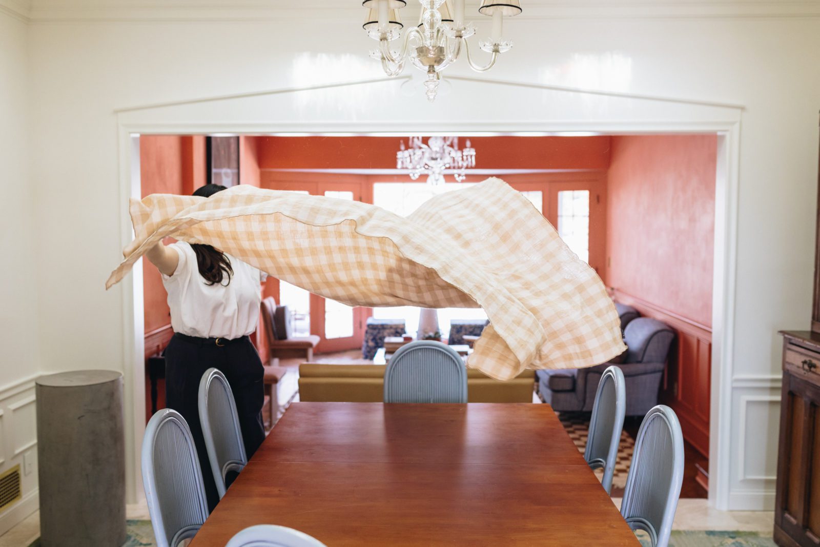 Woman is lifting a gingham tablecloth high in the air in preparation for setting a table.