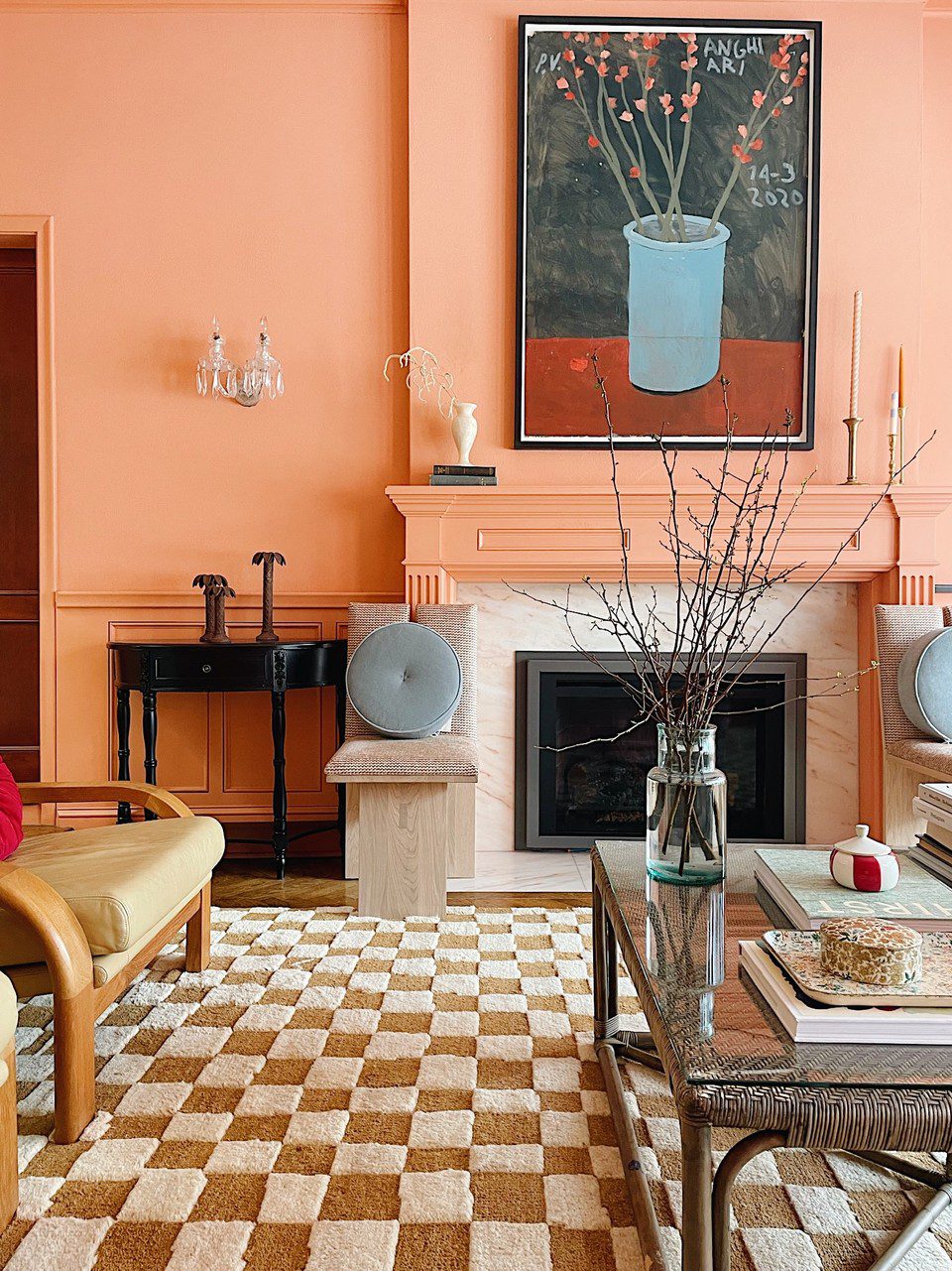 Peach living room with artwork over the fireplace, a checkerboard rug, and a woven coffee table with a glass top.