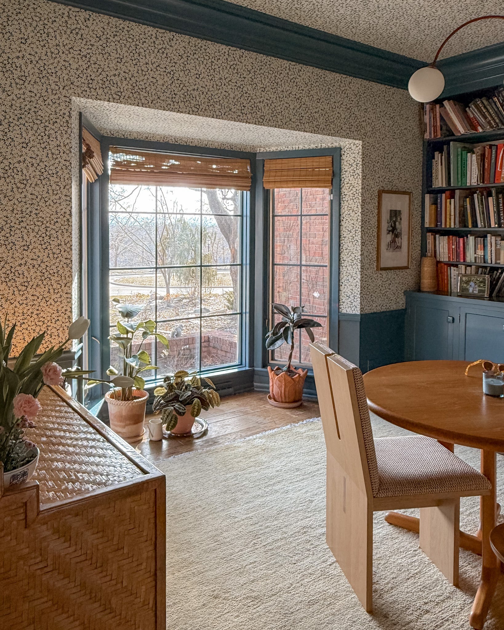 A cozy home office with blue woodwork, floral wallpaper, a neutral area rug, and a vintage desk