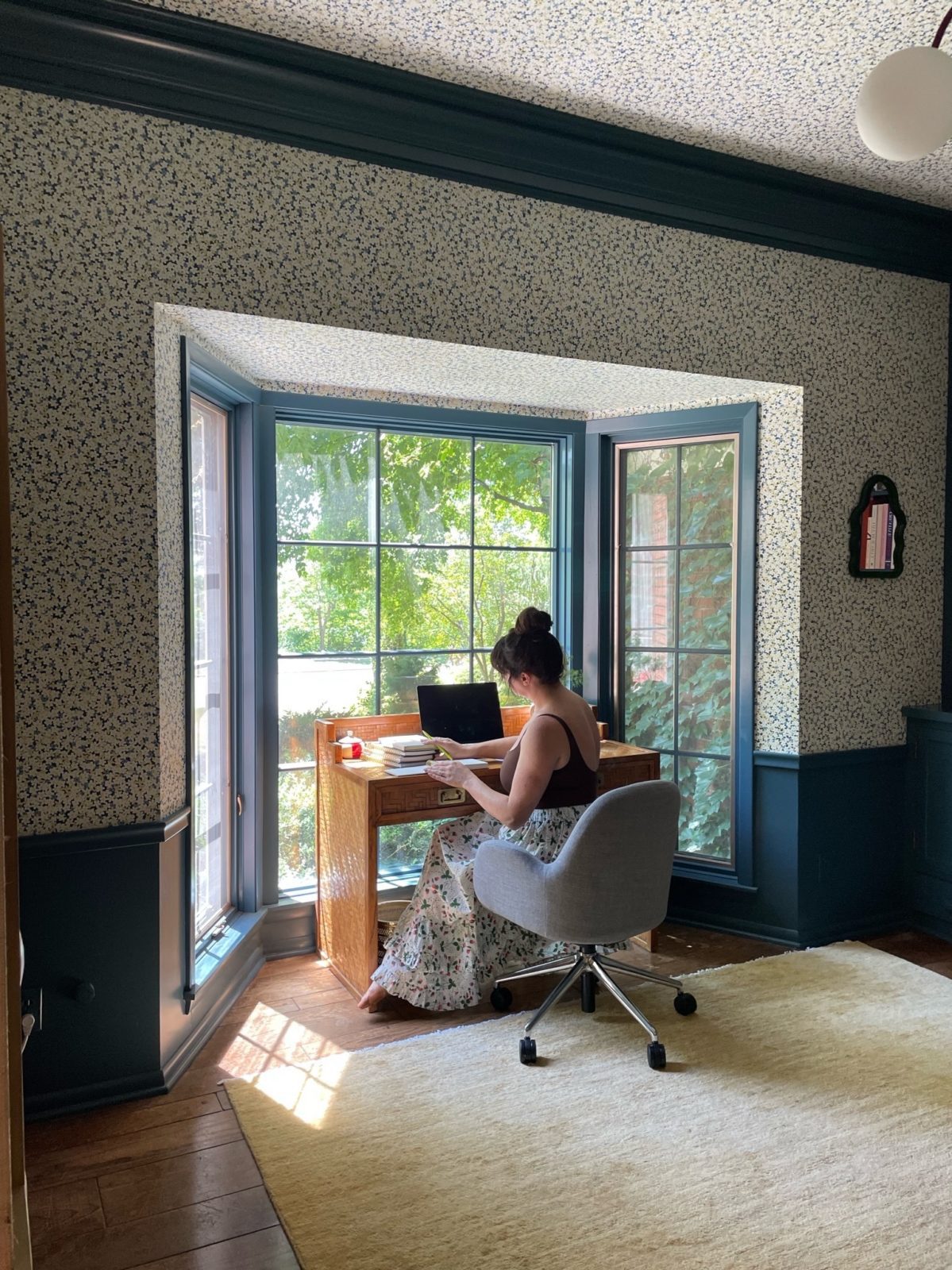 Woman sitting and working at a desk in a blue room in front of a window.