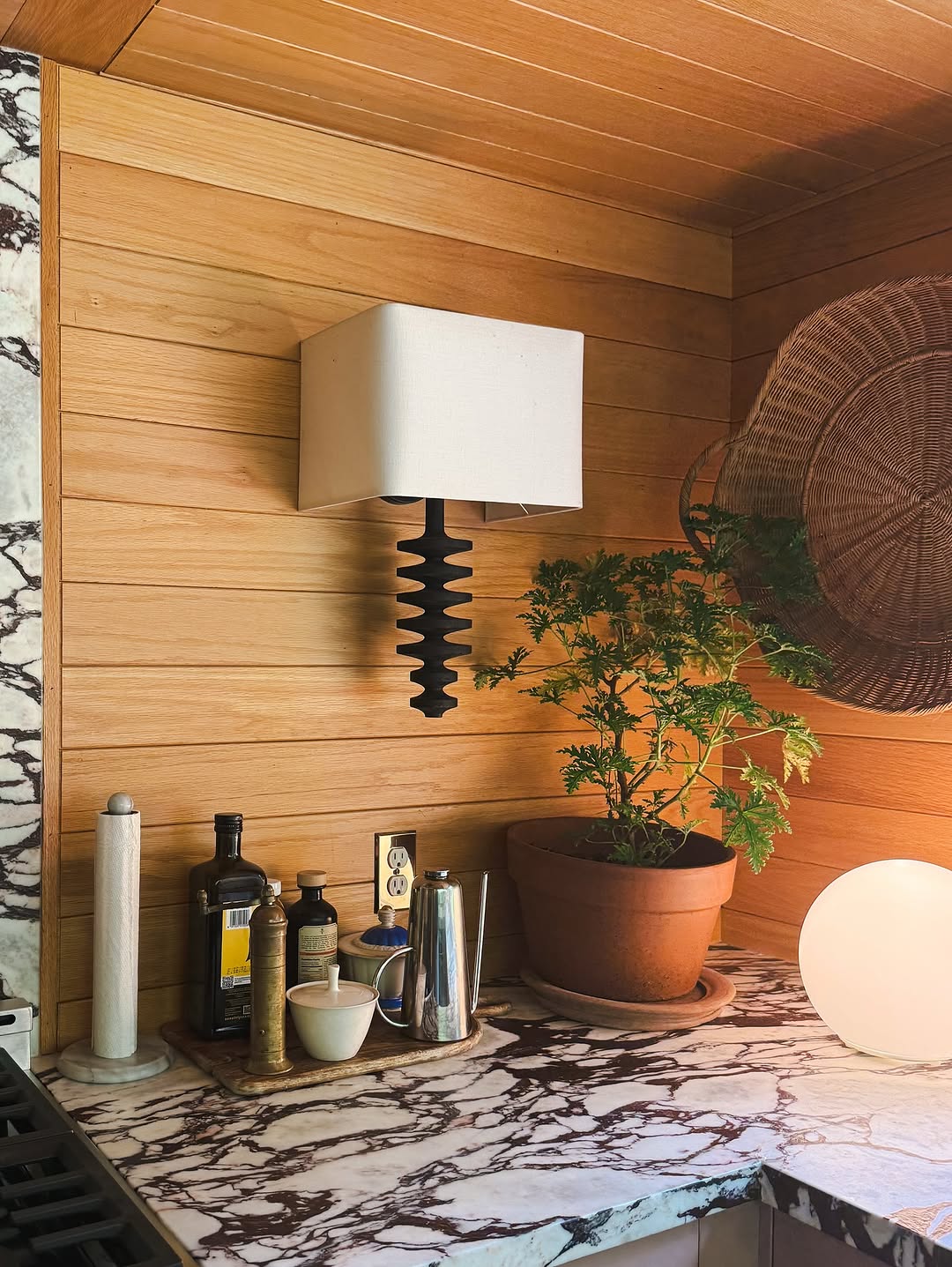 A kitchen corner with calacatta marble countertops, brown oak paneling, and a Regina Andrews black fishbone wall sconce