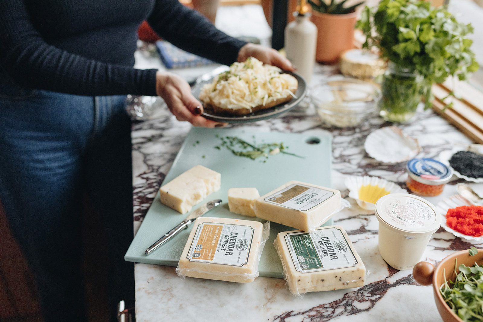 Woman prepares a meal in the kitchen with a variety of cheeses in the lead.