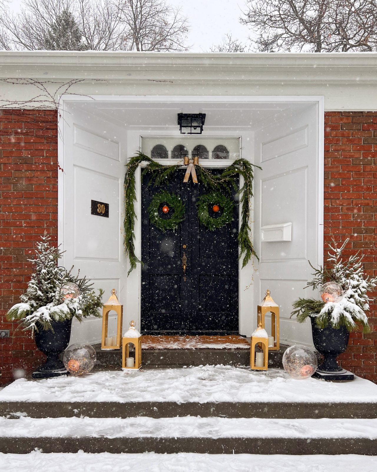 Snow falling in front of a festively decorated front door.