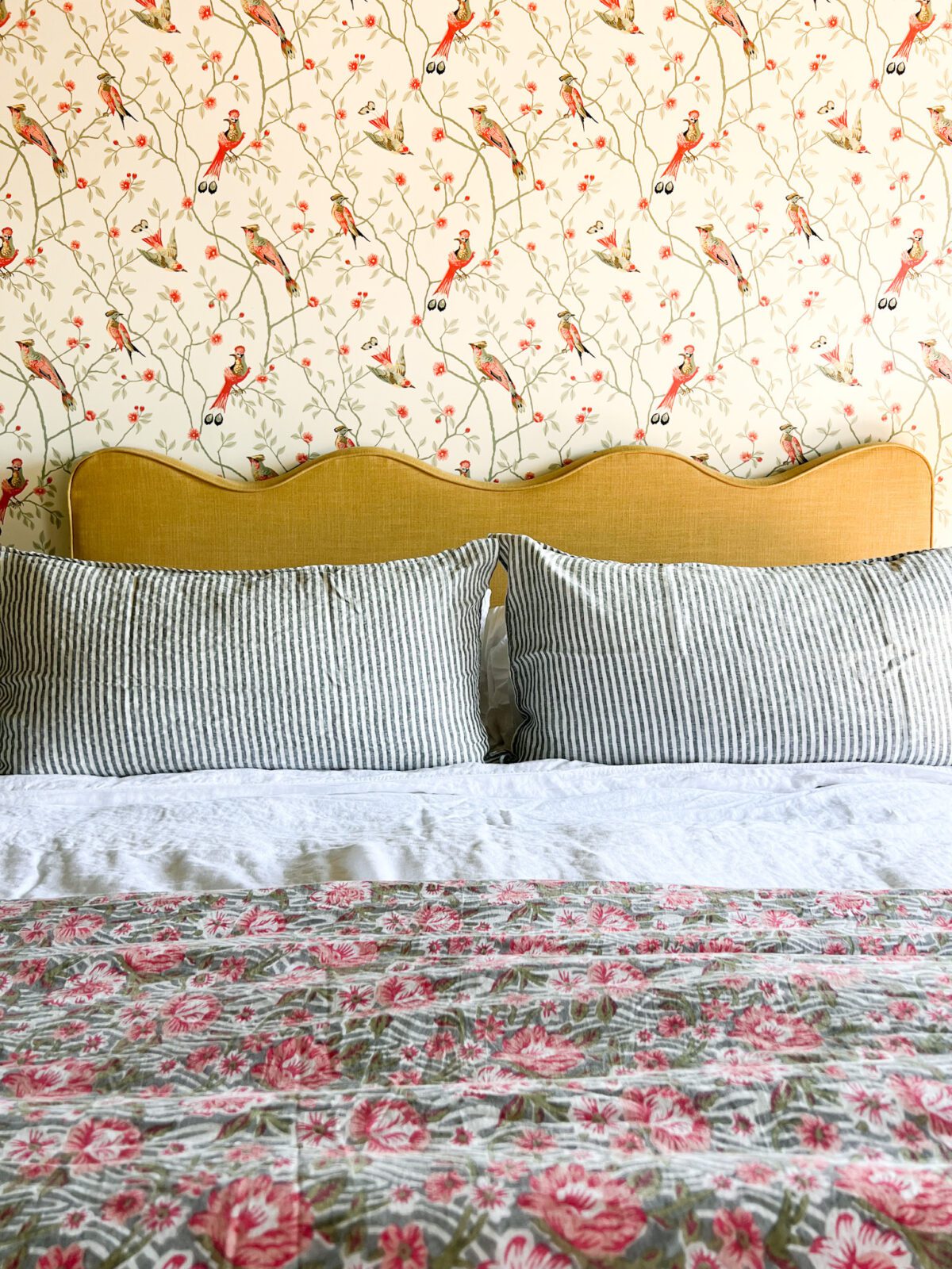 Tight view of a striped-patterned pillowcase, floral quilt and bird-patterned wallpaper.