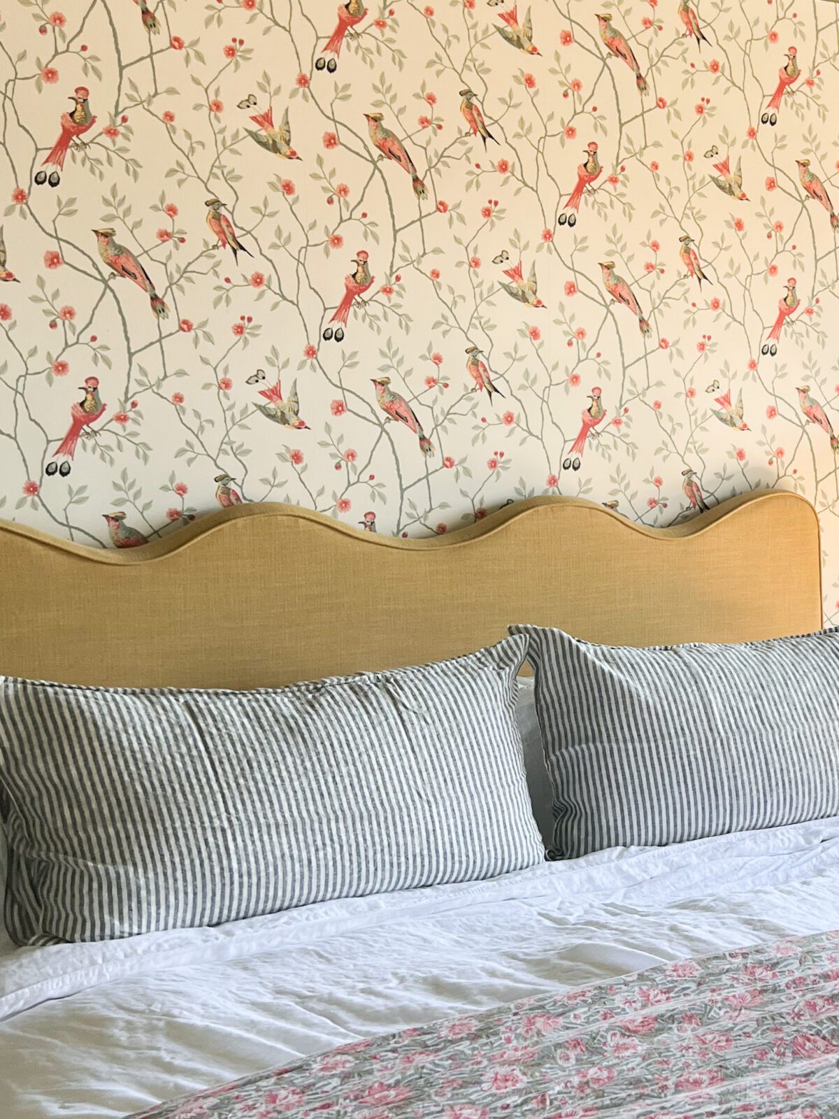 Close up view of bed pillows. The wallpaper, pillowcase, and quilt are patterned