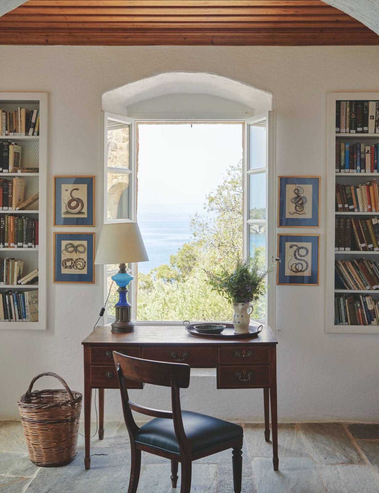 Patrick Leigh Fermor house. An antique wood desk sits in front of an open window and overlooks the sea in the distance.