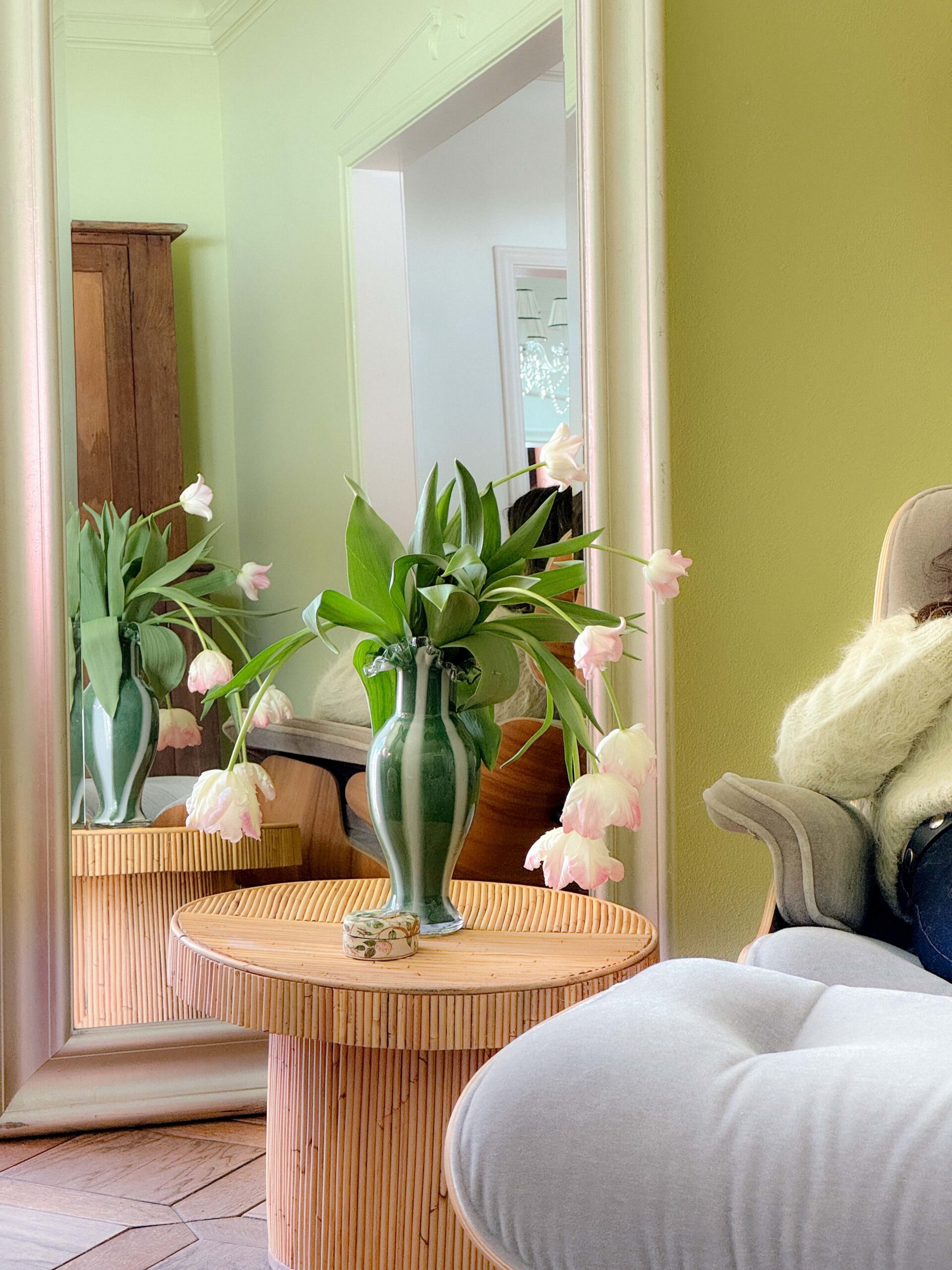 A striped green vase is filled with drooping pink tulips in a green-painted family room