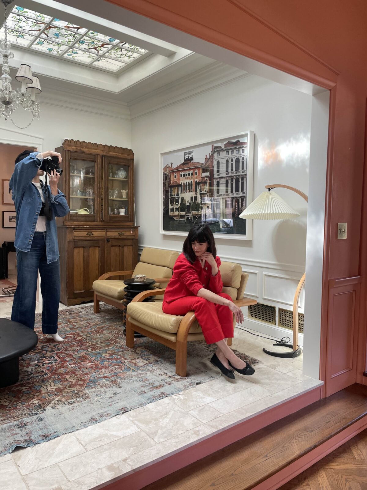 A woman is dressed in a cherry red pantsuit, posing on a vintage chair