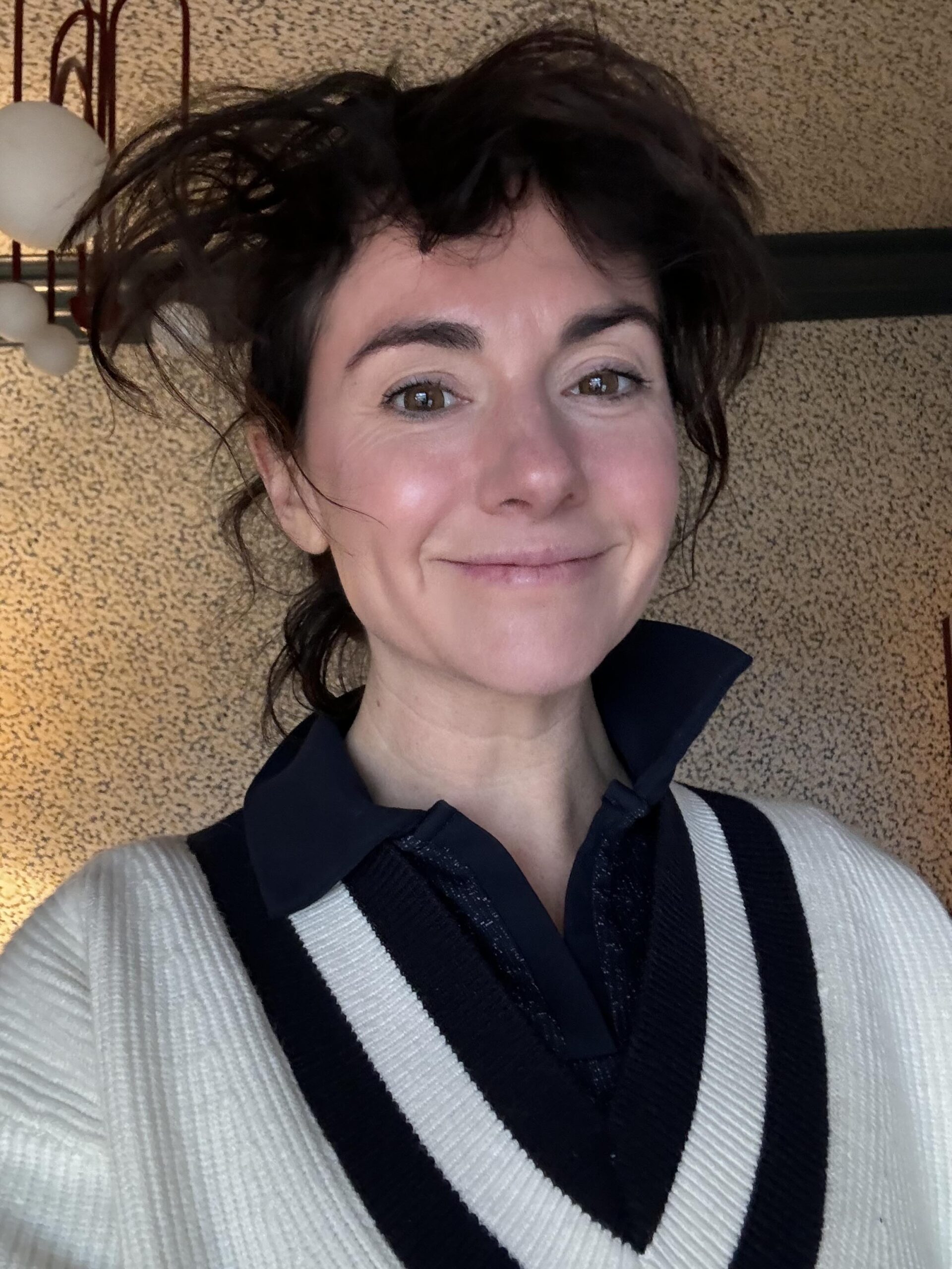 A woman poses for a selfie with messy hair and a smile on her face