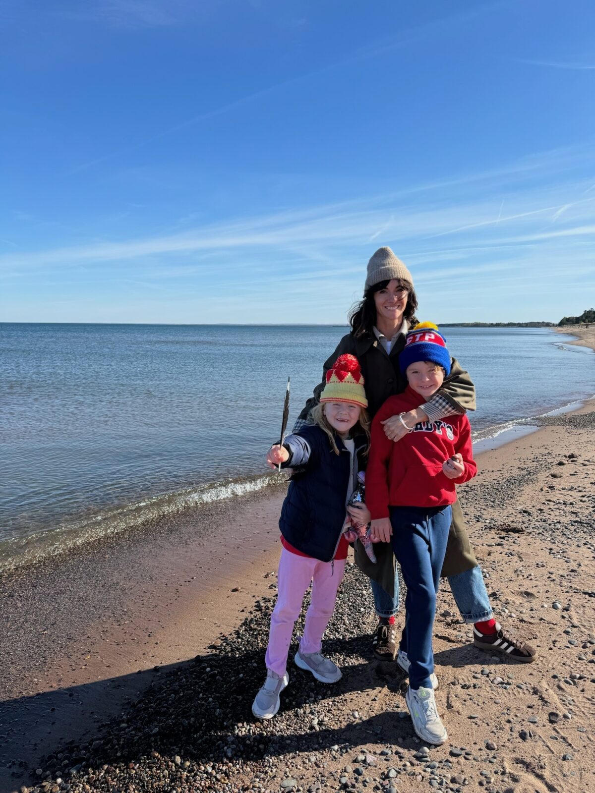 A mom and her two kids stand smiling on a beach in northern Minnesota in autumn
