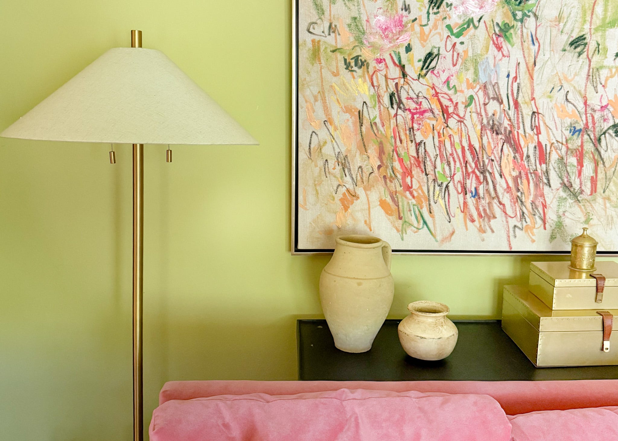 A pink sofa with a console table and floor lamp behind it, and abstract garden artwork from Anthropologie on the wall