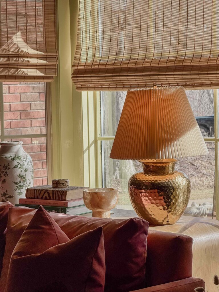 A gold lamp sits on a wood console table in front of a bay window