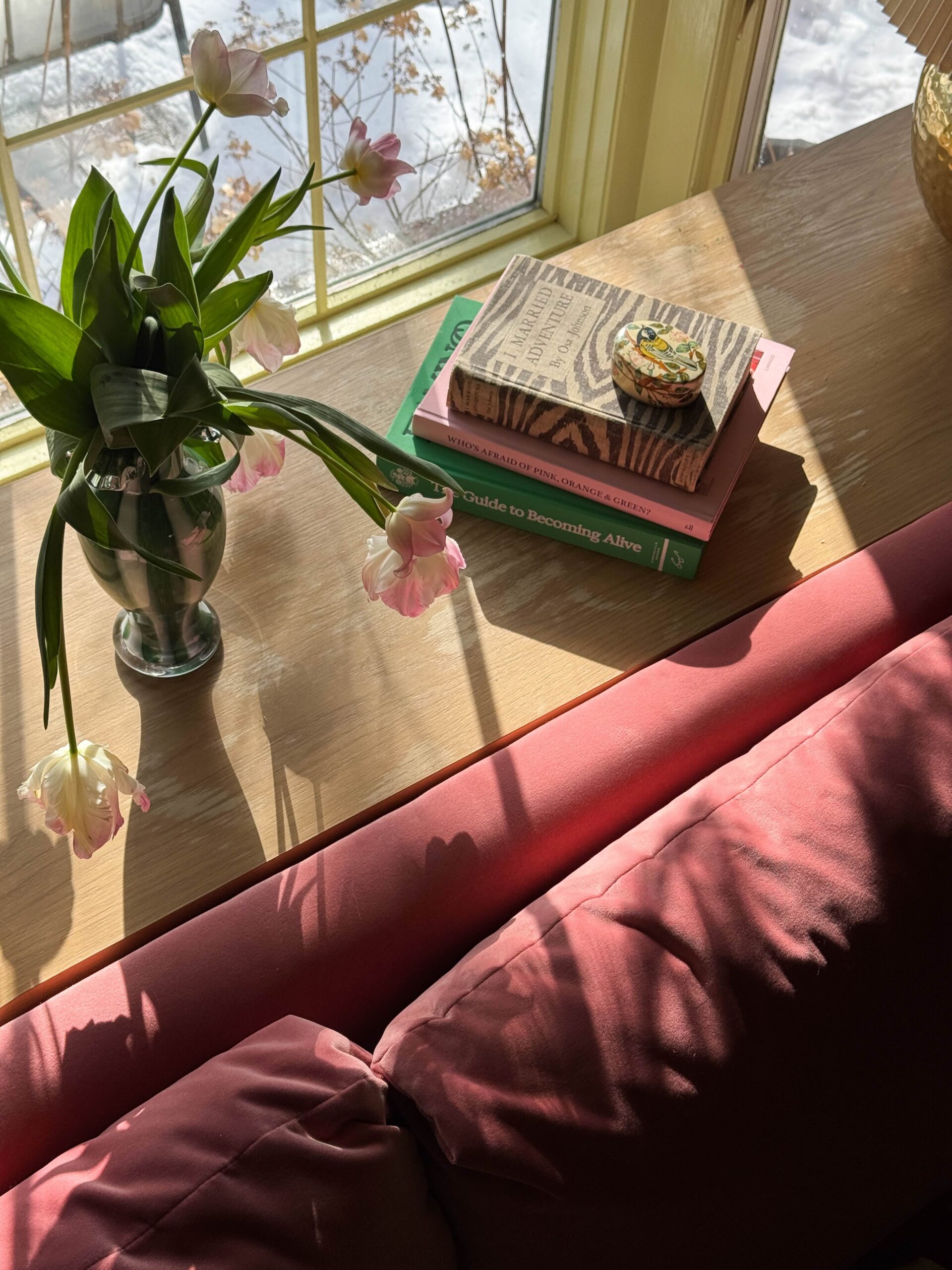 A pink sofa with a brown wood console table behind it, styled with tulips and a stack of books